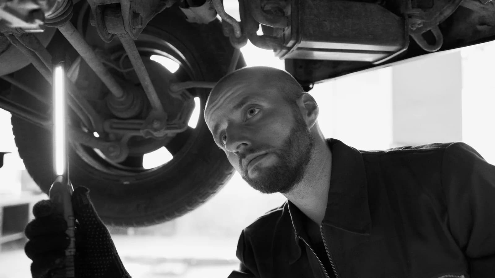 Mécanicien qui inspecte le train roulant et le dessous de caisse d'une voiture avec une lampe