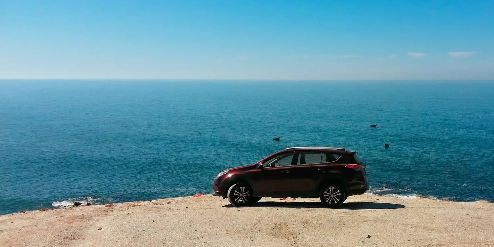 SUV sombre garé au bord d'une falaise face à la mer