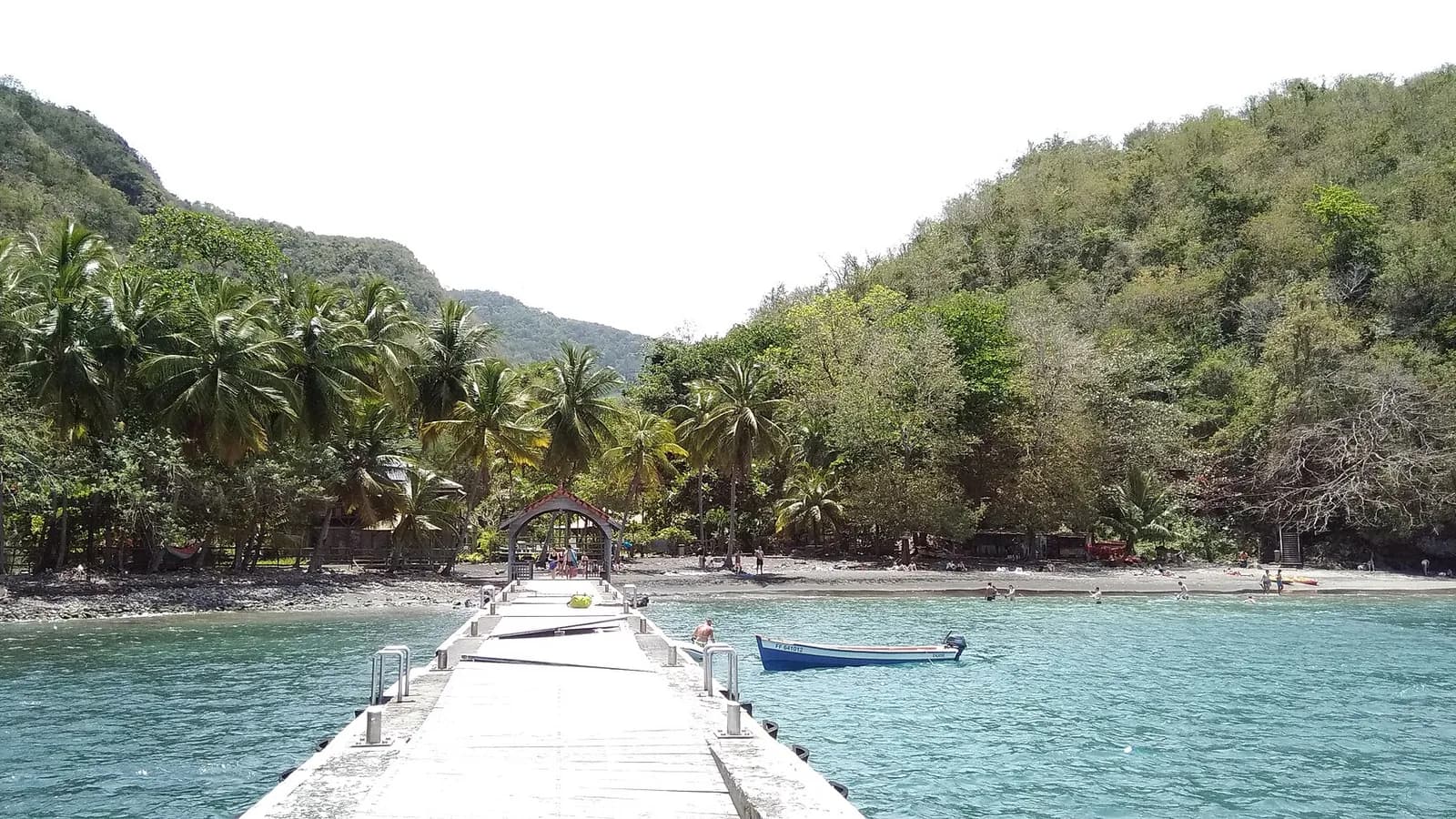 Ponton de l'Anse Noire bordé de cocotiers, avec une barque sur une eau turquoise
