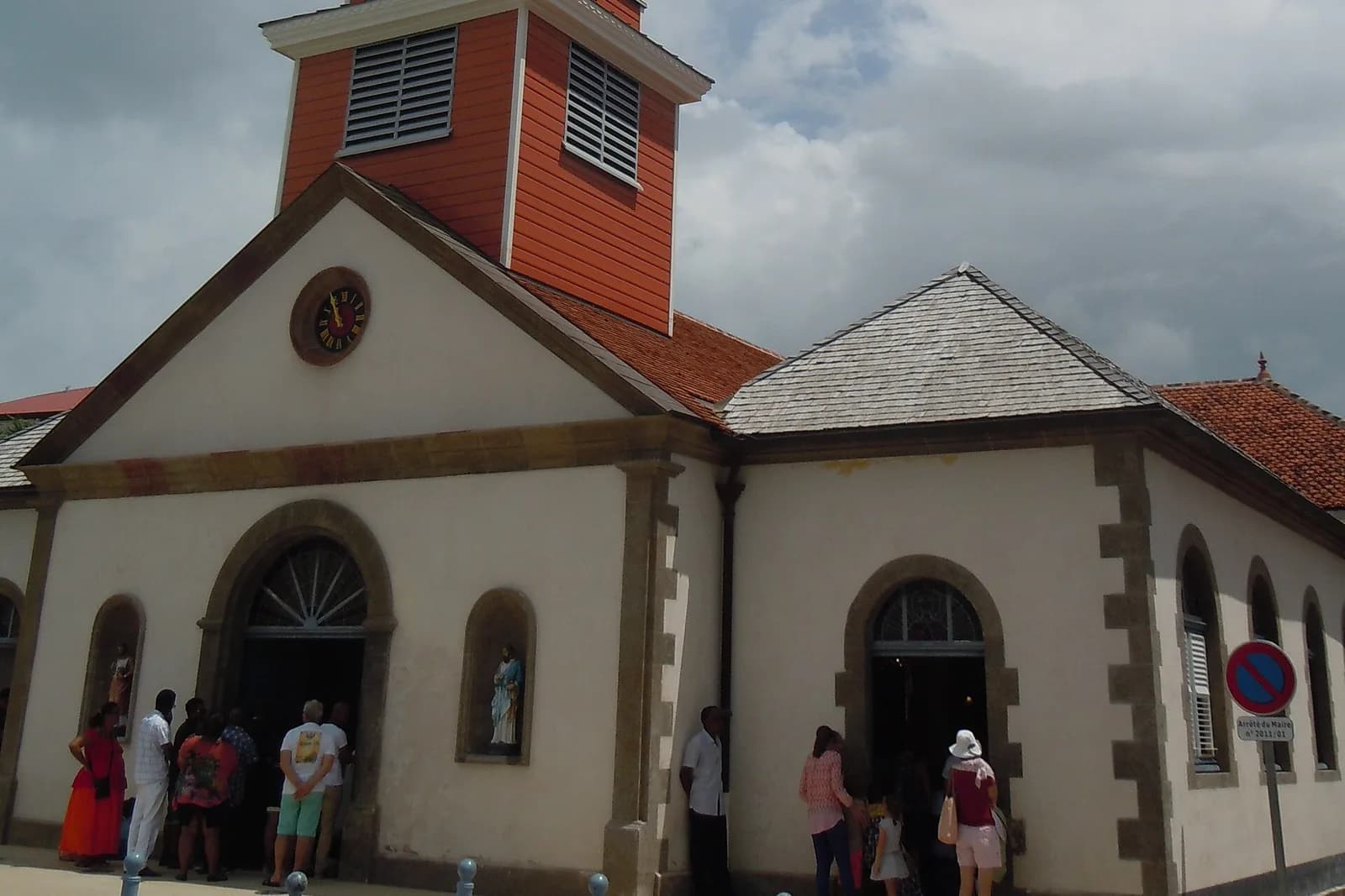 Façade de l'église Saint-Henri avec son clocher en bois, porches en arc et statue dans une niche