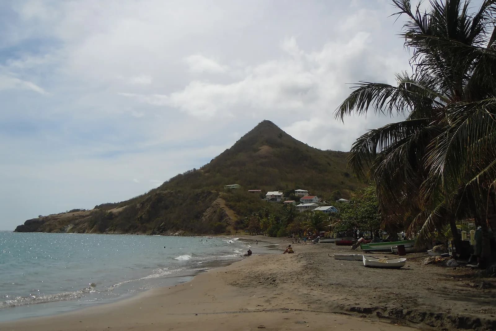 Plage de sable gris de Petite Anse, avec des barques de pêche échouées au pied d'un morne