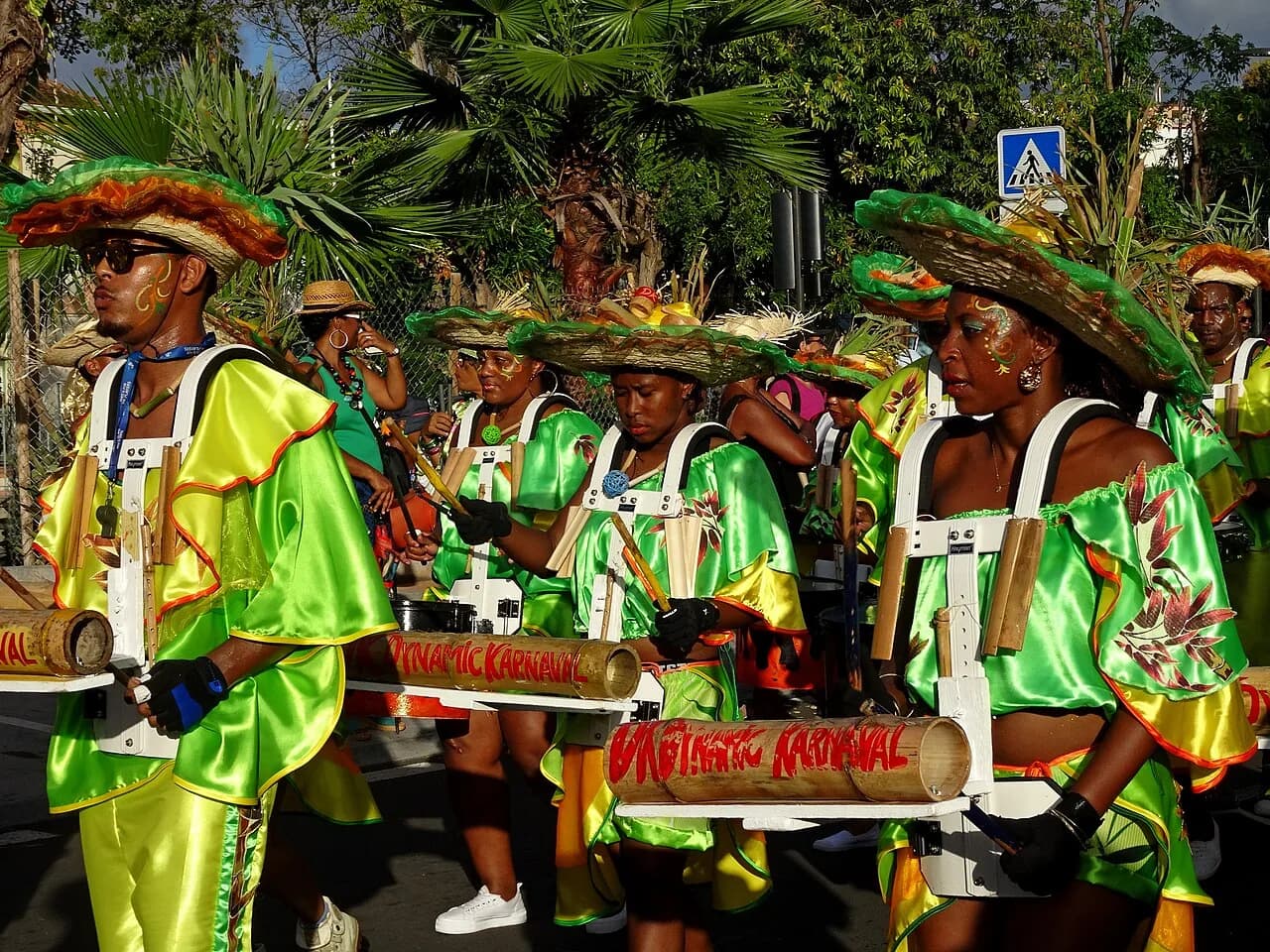 Groupe à pied costumé en vert et orange avec percussions en bambou lors d'un vidé du carnaval de Martinique