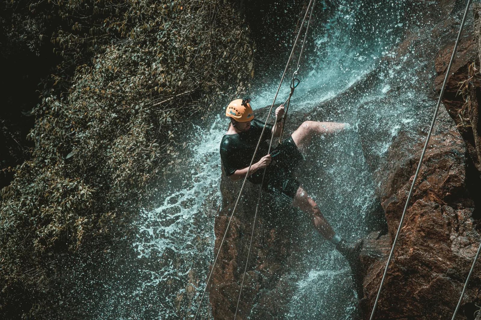 Canyoniste en descente en rappel le long d'une cascade en forêt tropicale