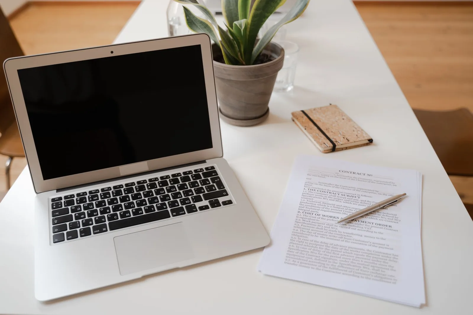 Ordinateur portable ouvert à côté d'un dossier de documents et d'un stylo sur un bureau blanc
