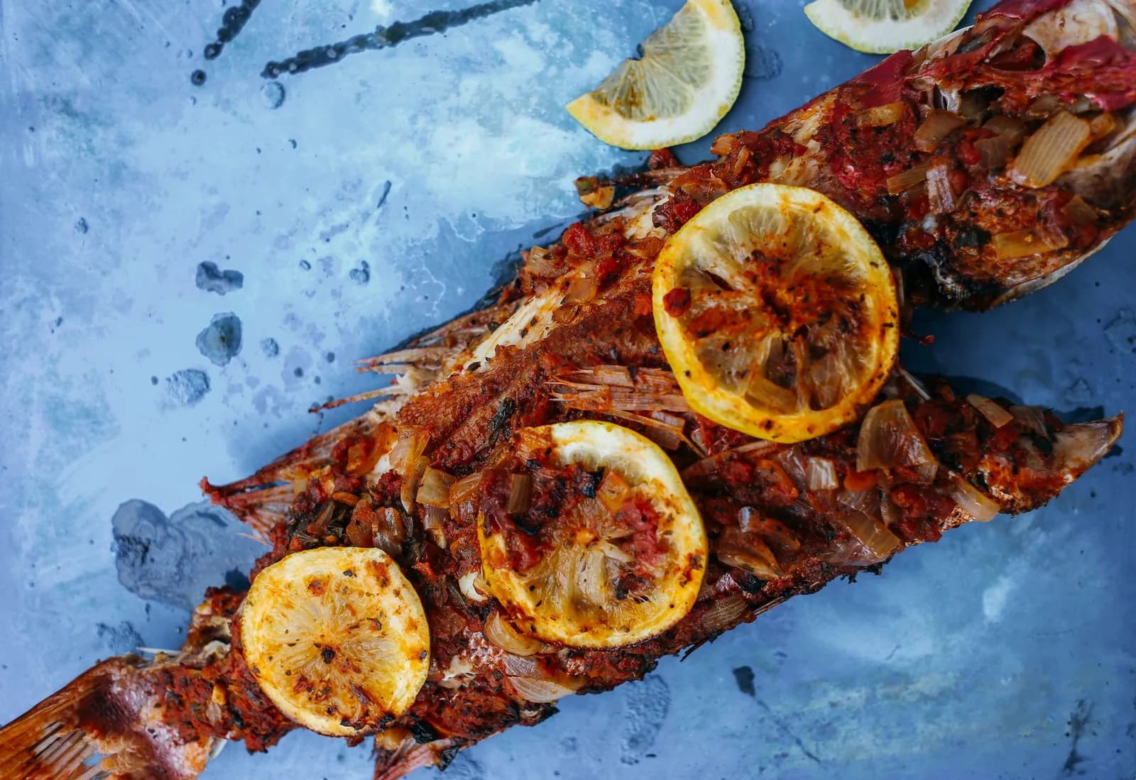Poisson entier nappé de sauce tomate pimentée aux oignons, garni de rondelles de citron