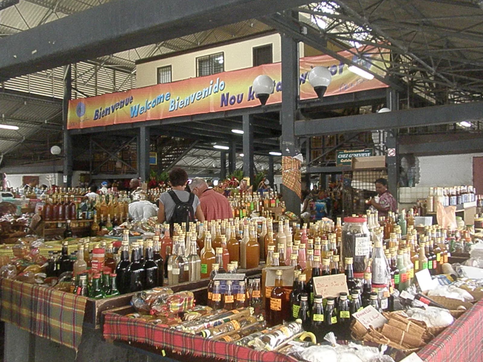 Étals du marché couvert de Fort-de-France chargés de rhums arrangés et de produits locaux, sous des nappes madras