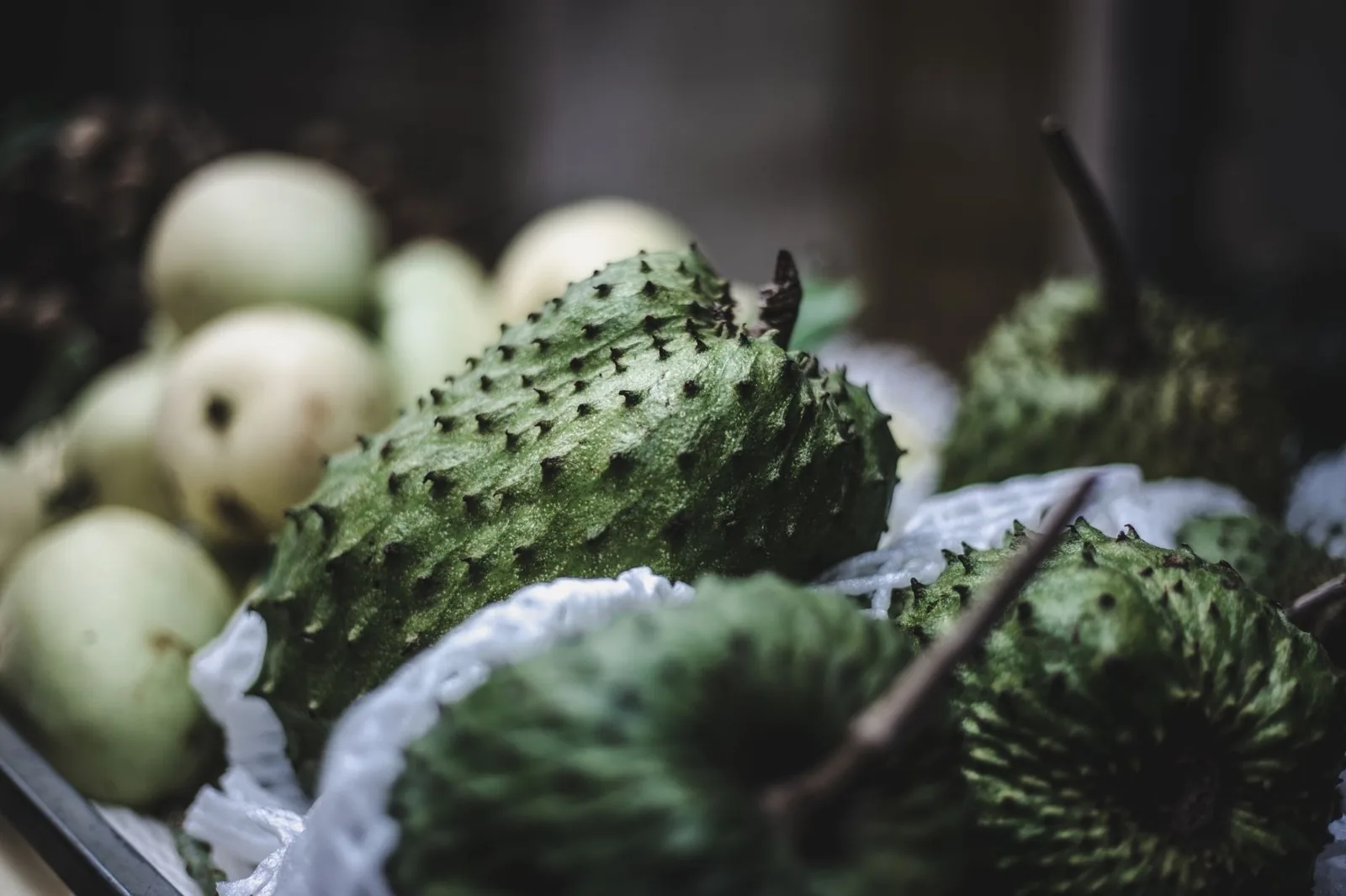 Corossols verts à pointes souples sur un étal, près d'autres fruits clairs