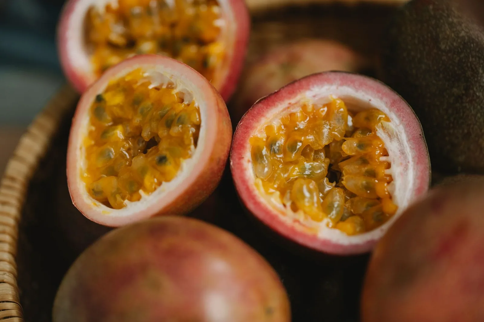 Fruits de la passion coupés en deux, pulpe orangée et graines noires, dans un panier