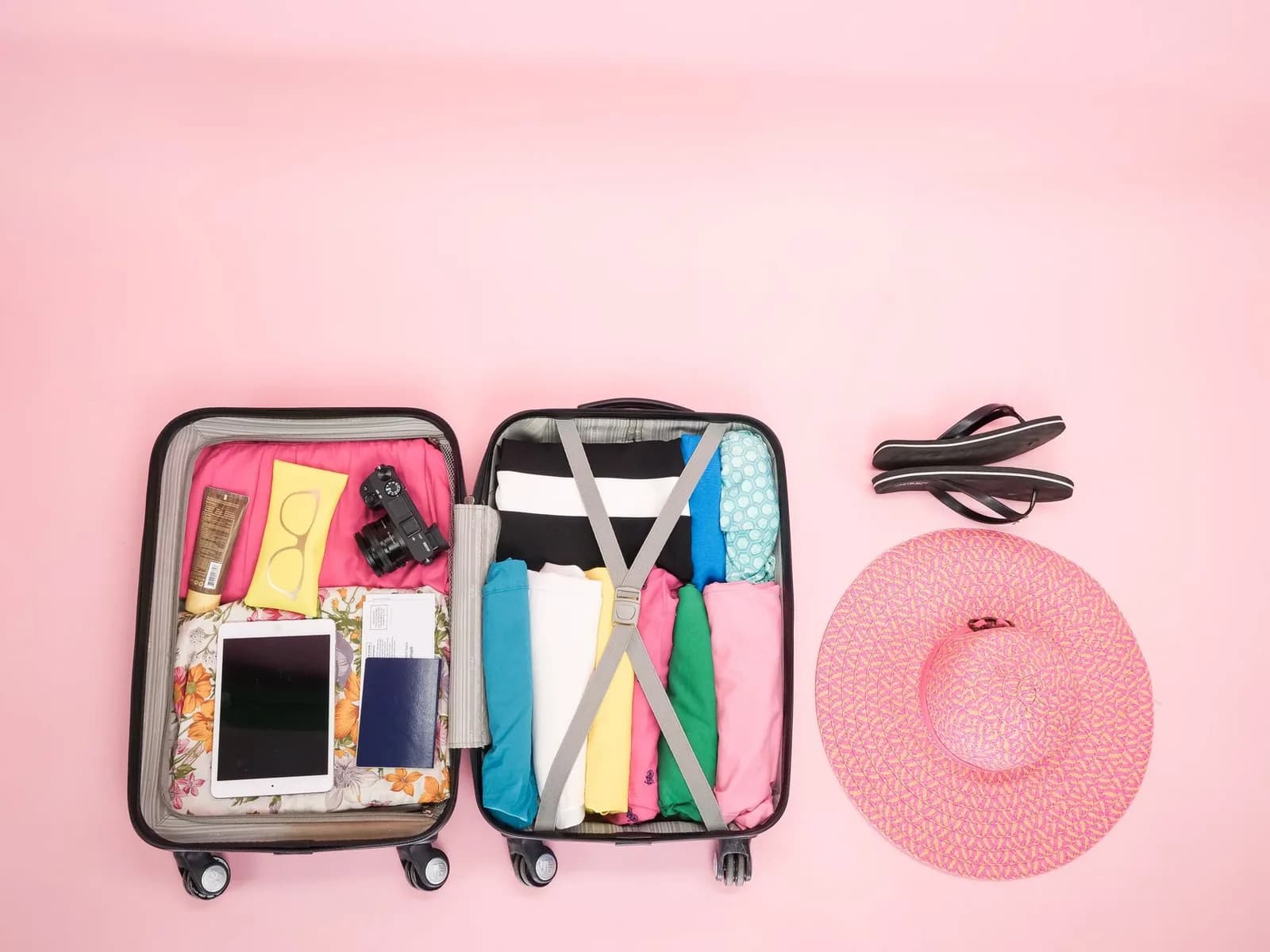 Valise ouverte vue du dessus avec chapeau de soleil, crème solaire, tongs, vêtements d'été et appareil photo