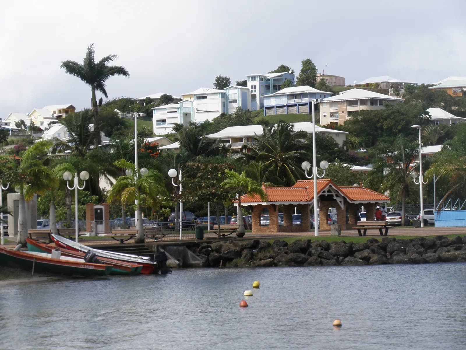 Quartier résidentiel sur la colline au-dessus de l'embarcadère des Trois-Îlets, avec maisons claires, palmiers et barques de pêche