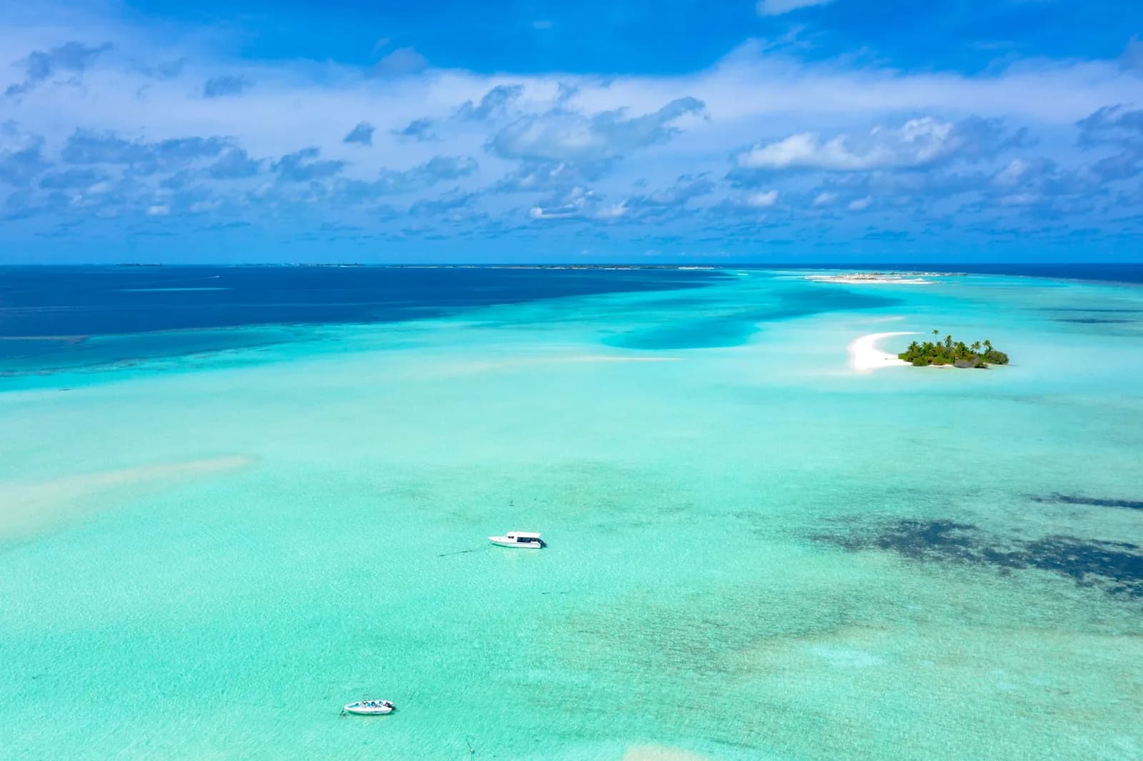 Fonds blancs turquoise peu profonds avec un petit îlet boisé et deux bateaux