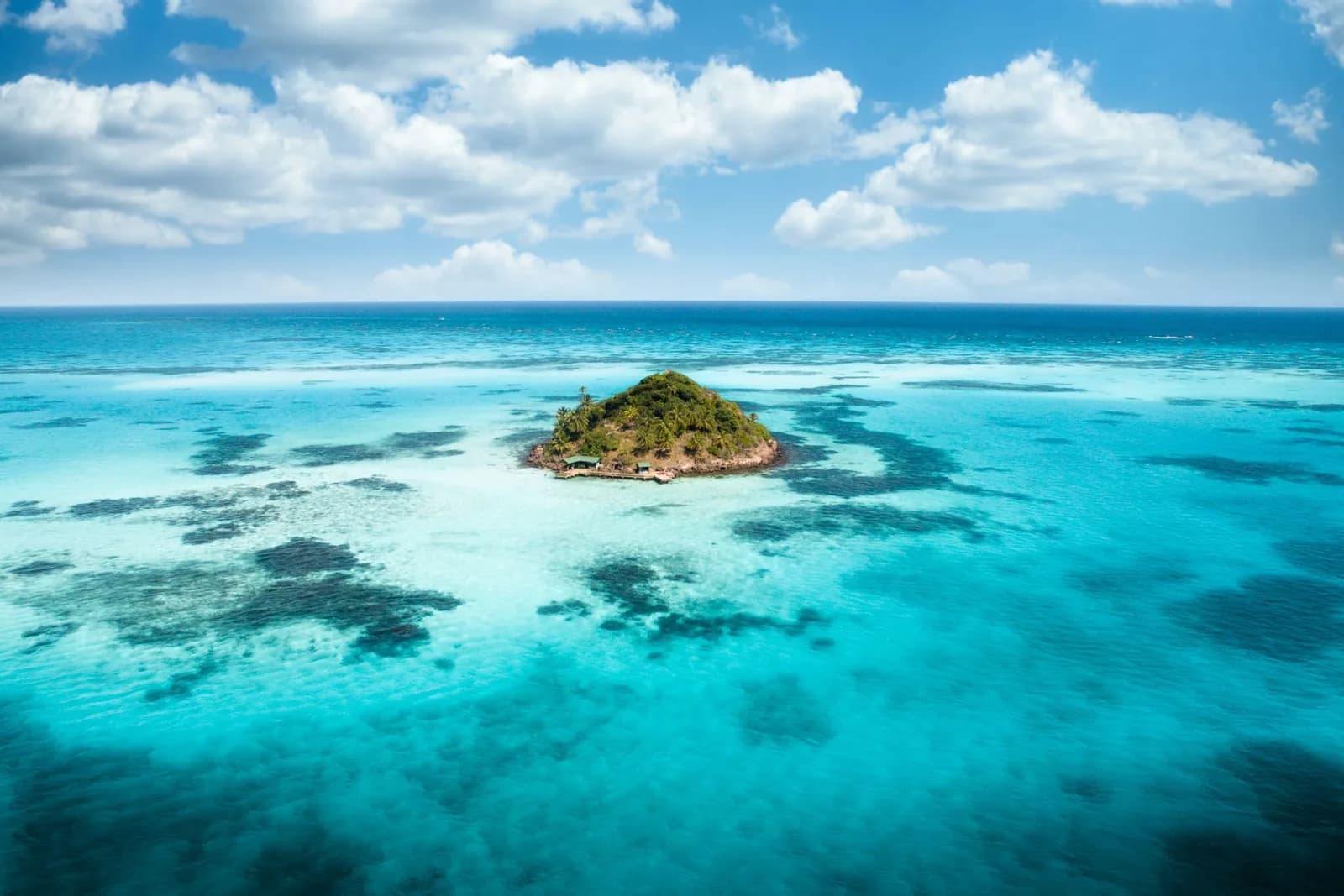 Vue aérienne d'un îlet tropical boisé entouré d'eaux turquoise peu profondes