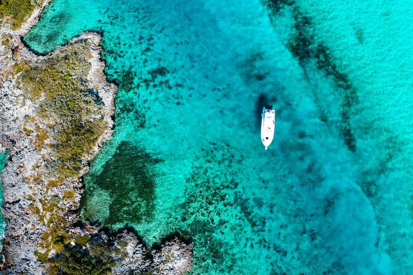 Vue aérienne d'une côte rocheuse couverte de végétation et d'un petit bateau blanc sur eau turquoise
