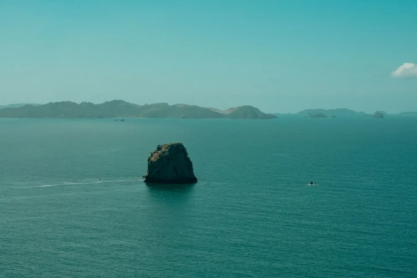 Rocher isolé émergeant d'une mer calme, au large d'une côte montagneuse