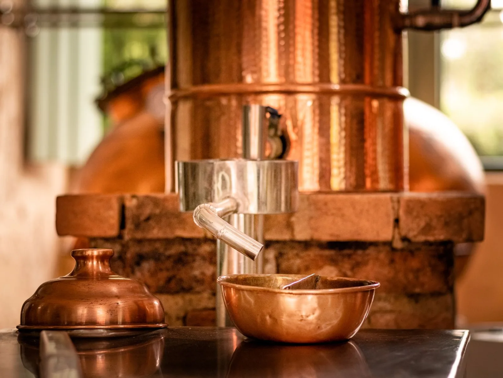 Alambic en cuivre et petit bol de cuivre devant un muret de briques dans une distillerie de rhum