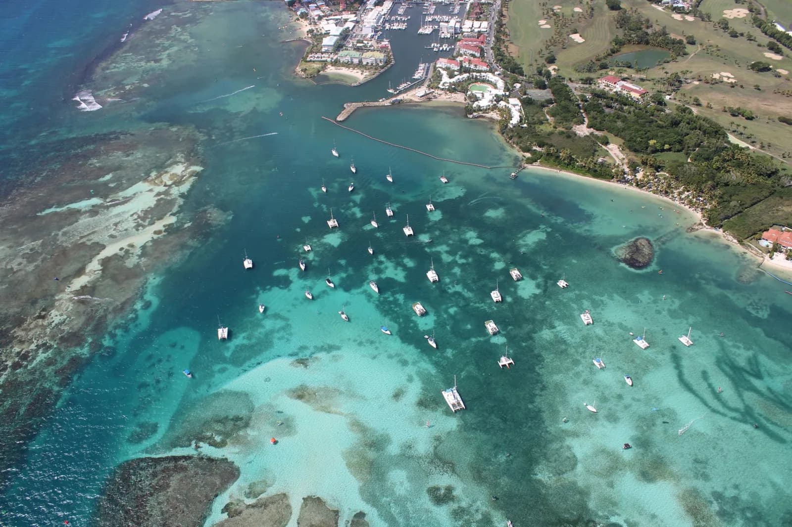Vue aérienne d'une baie aux eaux turquoise, récifs et voiliers mouillés, aux Antilles