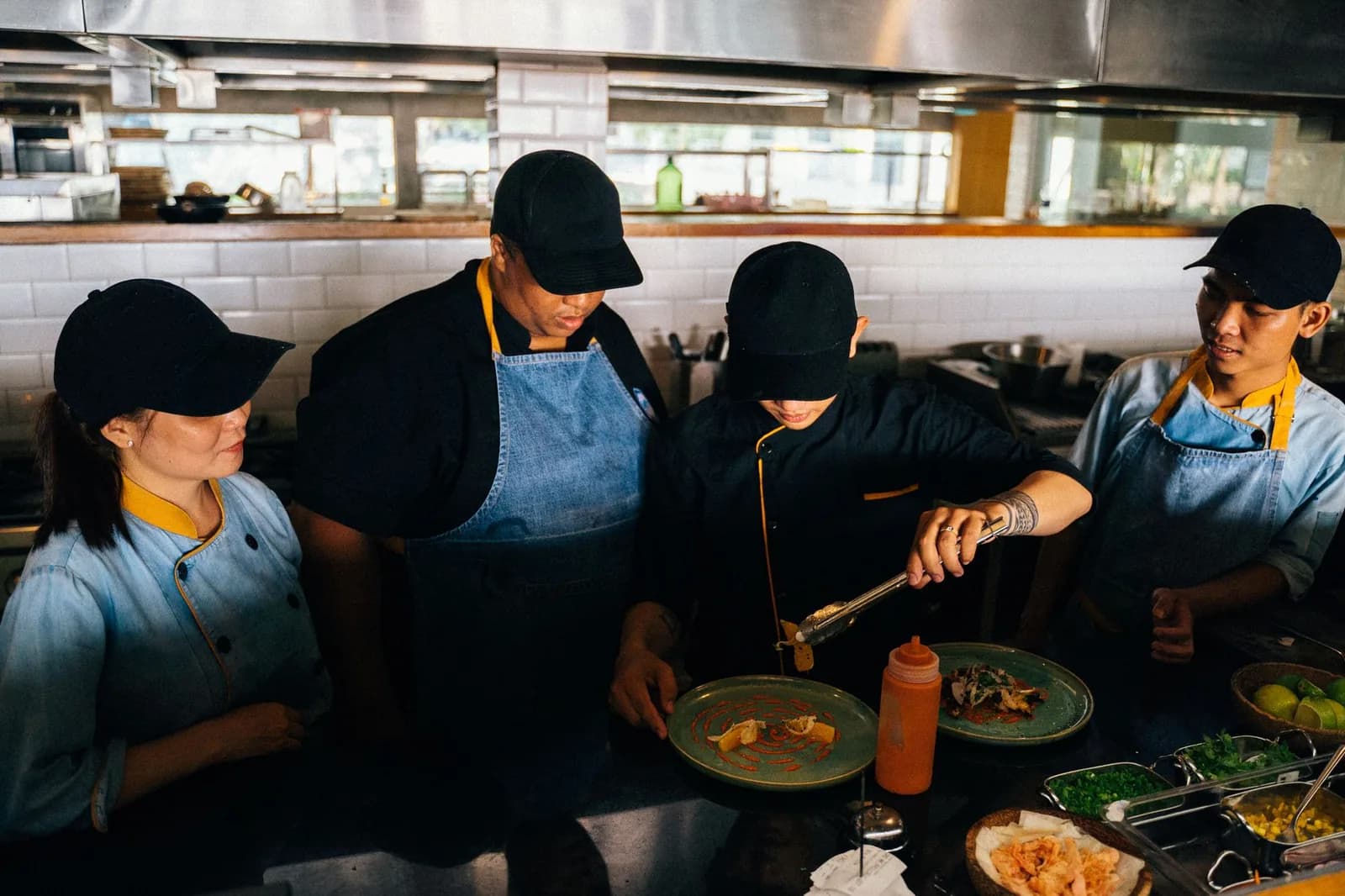 Équipe de quatre cuisiniers en tablier dressant des assiettes dans une cuisine ouverte de restaurant