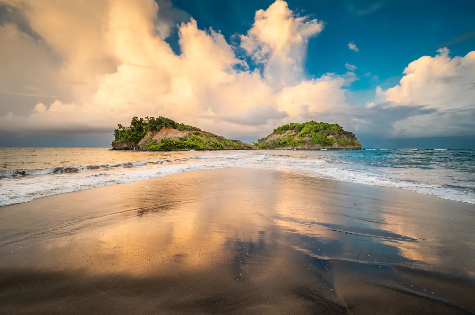 Plage de sable noir à Sainte-Marie, en Martinique, face à deux îlots verdoyants au coucher du soleil