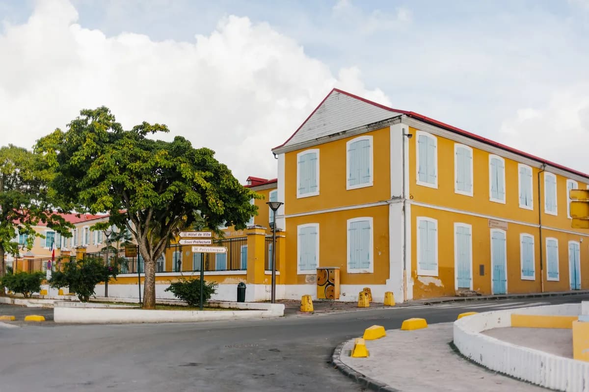 Bâtiment colonial jaune à volets bleus au coin d'une rue ensoleillée