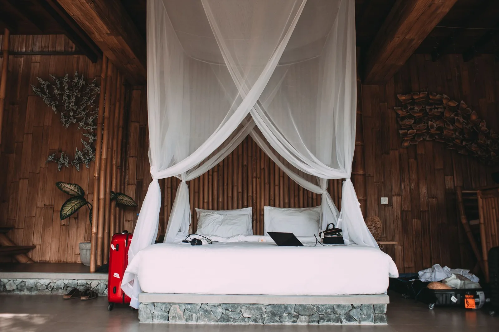 Lit double sous une moustiquaire blanche dans une chambre en bois et bambou