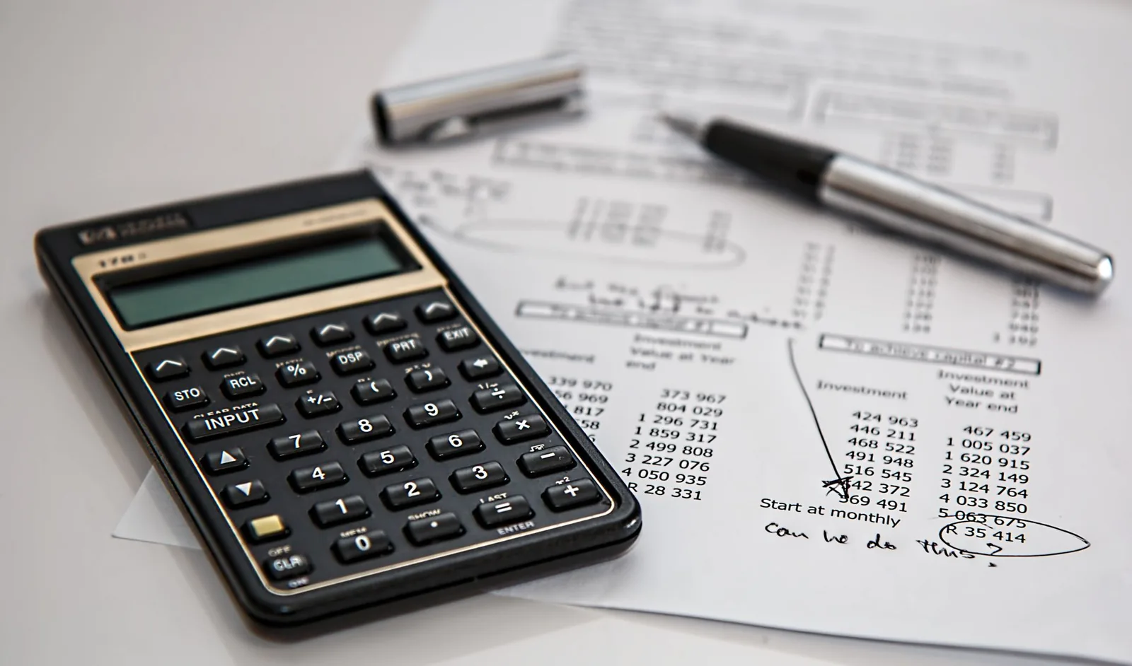Calculatrice noire posée sur une feuille de chiffres, avec un stylo