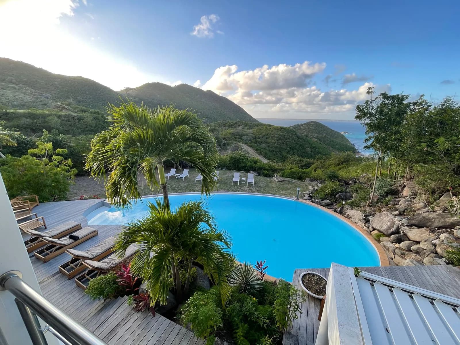 Piscine à débordement d'un hébergement avec transats, collines vertes et mer des Caraïbes à l'horizon