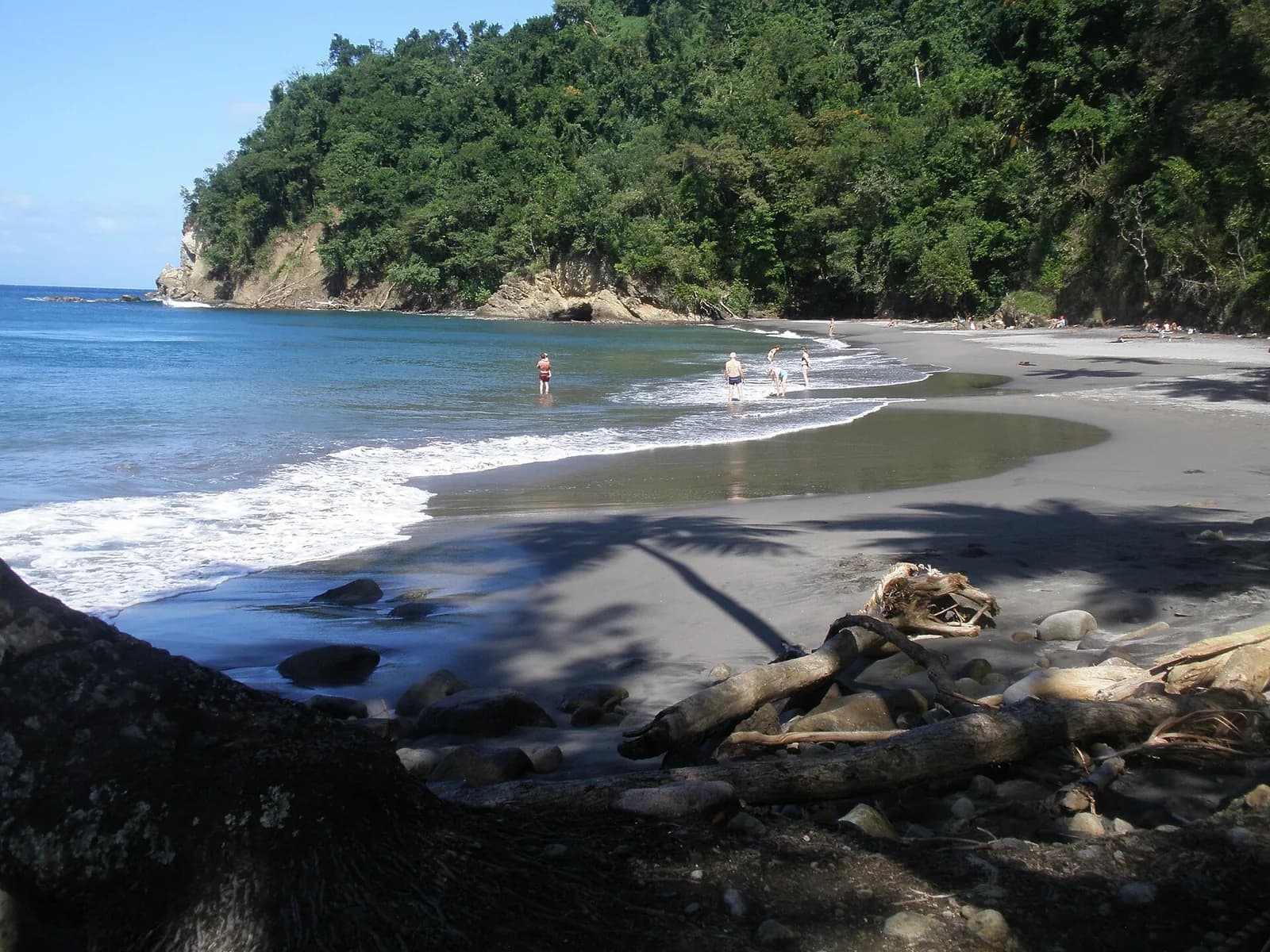 Plage de sable noir de l'Anse Couleuvre au Prêcheur, bordée de forêt, avec quelques baigneurs