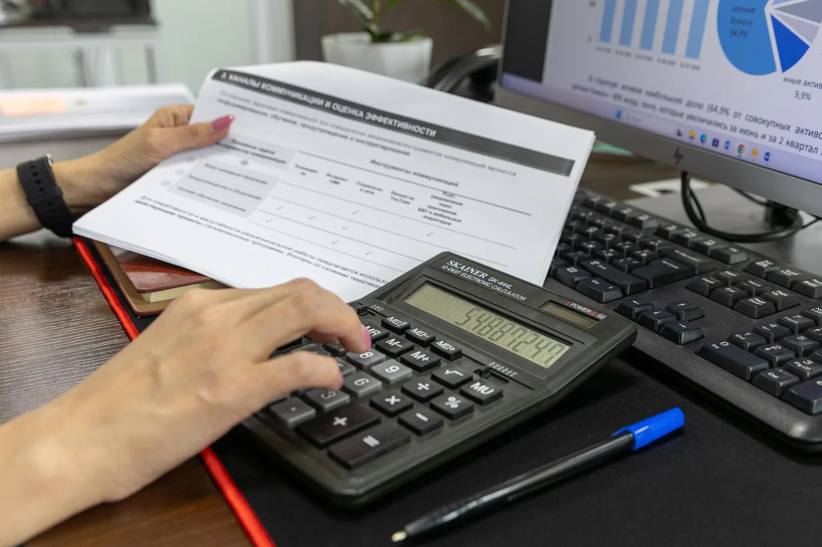 Mains sur une calculatrice, avec un document imprimé et un ordinateur sur un bureau