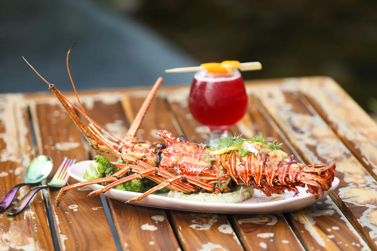 Langouste grillée servie en assiette sur une table en bois, avec un cocktail rouge, cuisine des Antilles