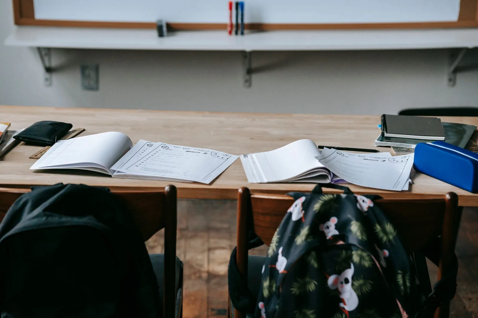 Cahiers ouverts et trousse sur un bureau d'école, avec deux cartables posés sur les chaises