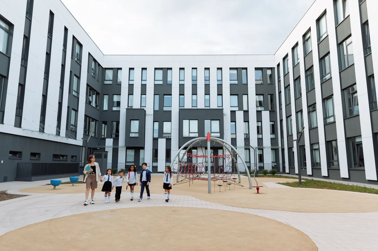 Élèves en uniforme et une enseignante marchant dans la cour d'un établissement scolaire moderne