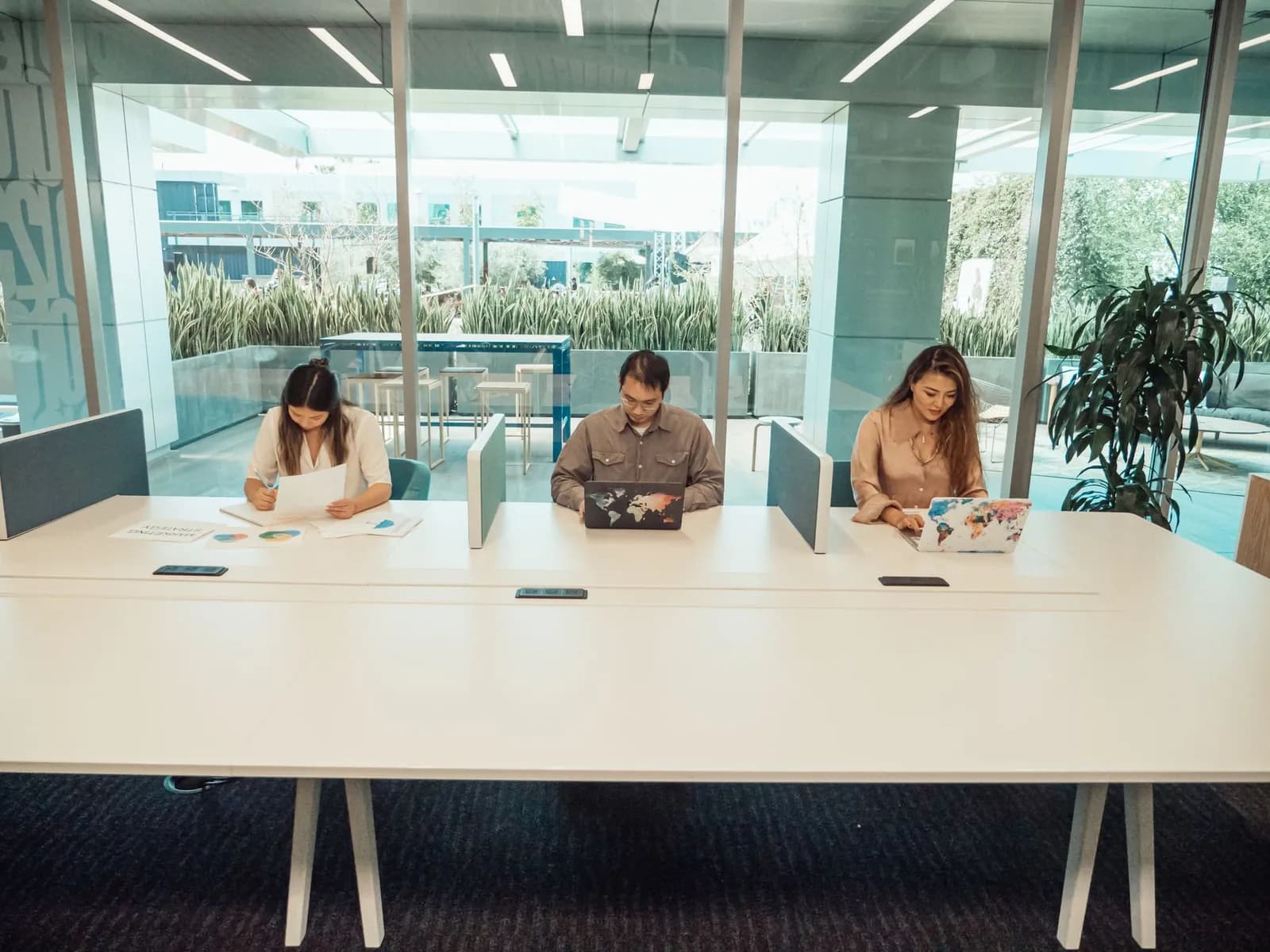 Trois personnes travaillant sur ordinateur portable autour d'une grande table dans un espace de coworking lumineux