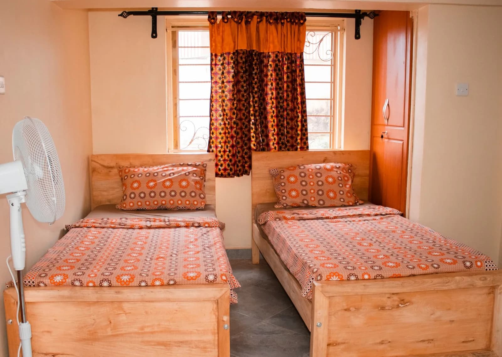 Chambre meublée avec deux lits simples, un ventilateur et des rideaux colorés