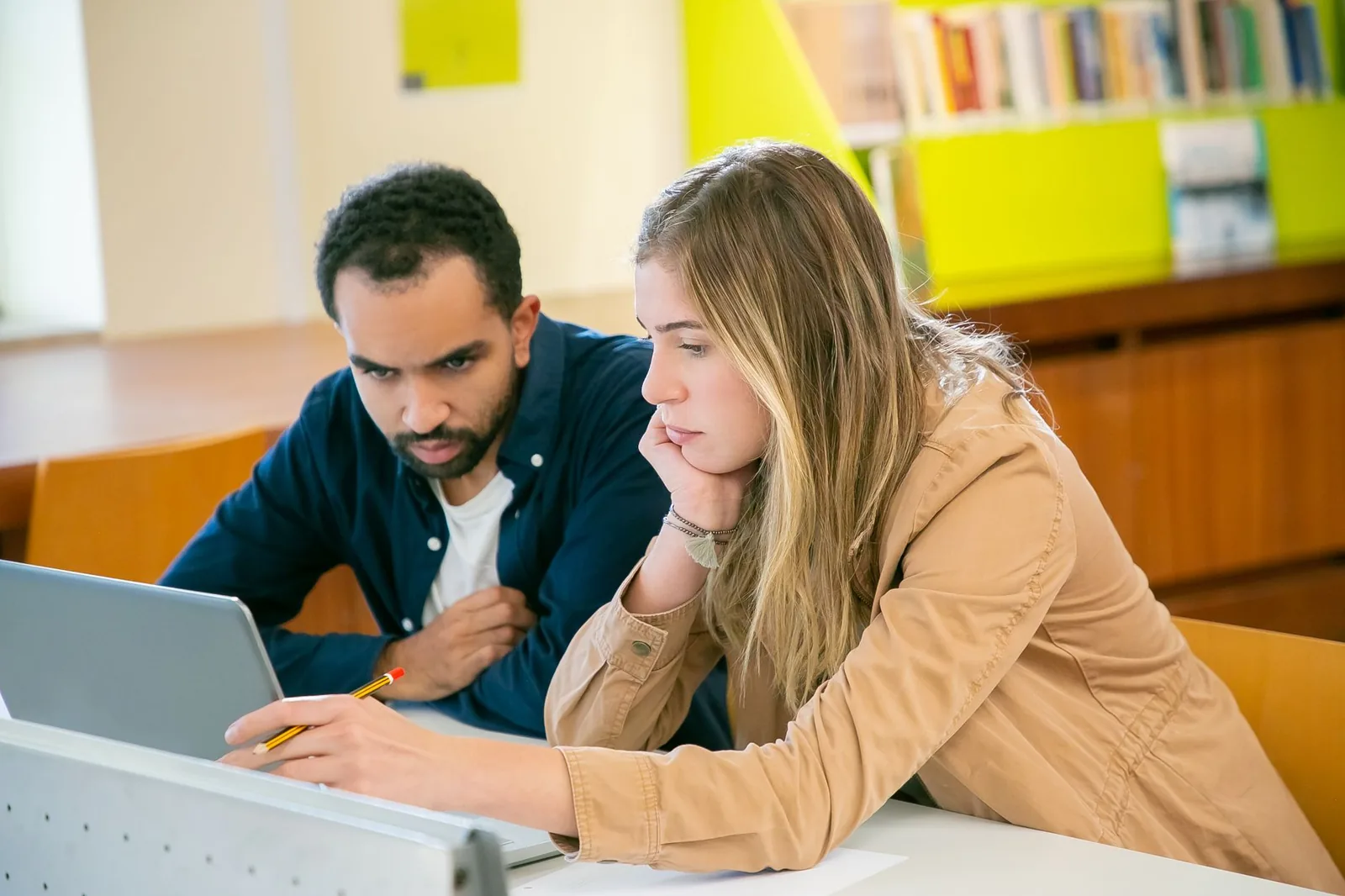 Deux étudiants penchés sur un ordinateur portable dans une bibliothèque universitaire